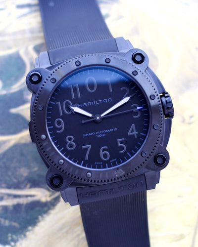 Hamilton watch with blue strap and dark face on a blurred natural background