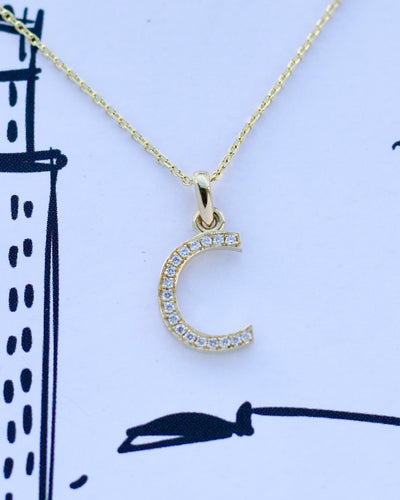 Gold necklace with a C with diamonds pendant on a white background with black line art.