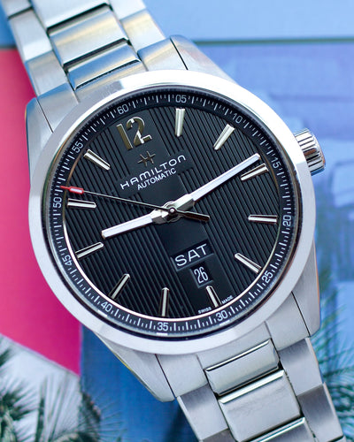 Hamilton watch with black dial and silver metal strap on a colorful background