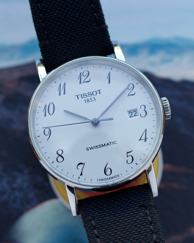 Tissot watch with black strap and white dial against a blurred natural background