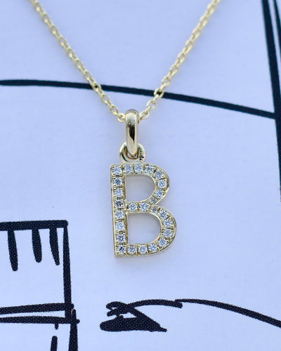 Gold necklace with a 'B' pendant on a light blue background