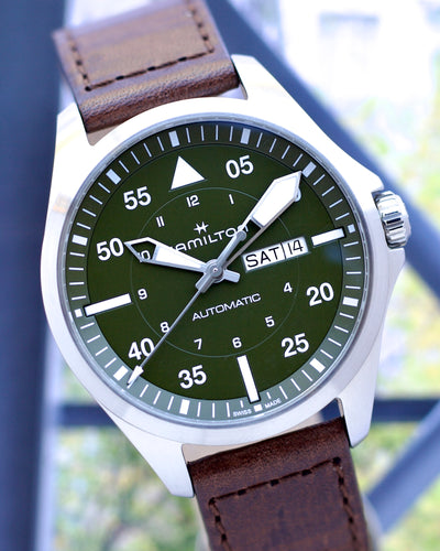 Hamilton watch with green dial and brown leather strap against a blurred outdoor background