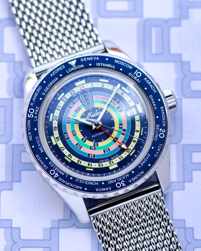 Wristwatch with a detailed face showing time zones on a blue geometric patterned background