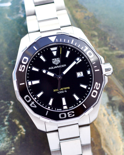 Silver TAG Heuer Aquaracer watch with black dial on a blurred natural background