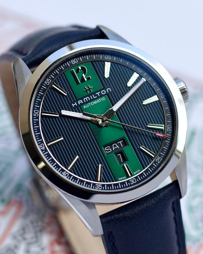 Hamilton watch with blue strap and green and black face on a blurred background