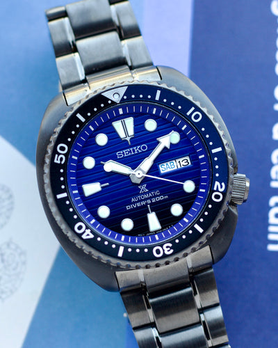 Seiko watch with blue dial and silver metal strap on a blue background