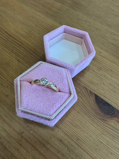Gold ring with a diamond in a pink hexagonal jewelry box on a wooden surface
