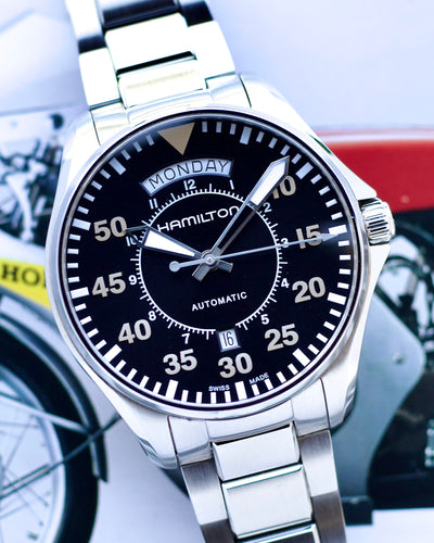 Hamilton watch with black dial and silver metal strap on a blurred background