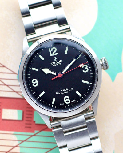 Tudor watch with black dial and silver metal strap on a colorful background