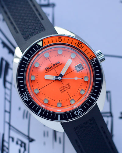 Bulova watch with orange face and black strap on a blurred background