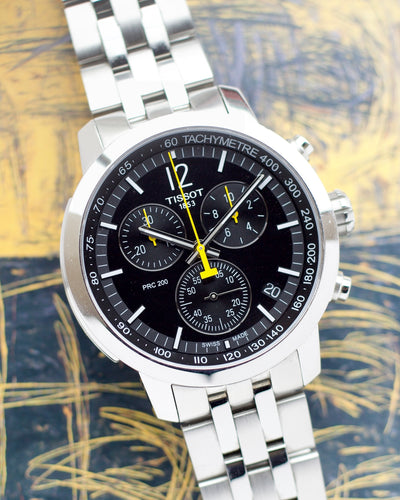 Silver Tissot watch with black dial on a textured yellow and blue background