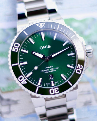 Oris watch with green face and silver case on a blurred map background