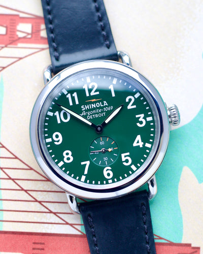 Shinola watch with green face and blue strap on a colorful background