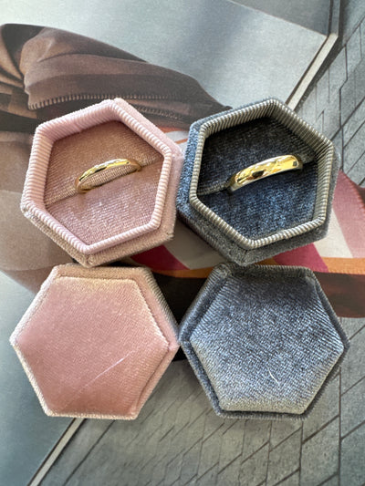 Hexagonal jewelry boxes in various colors with rings inside on a textured surface.