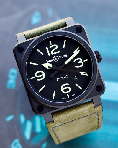Bell & Ross watch with black dial and green strap on a blurred blue background