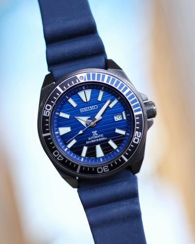 Seiko black steel watch on blue dial and rubber band