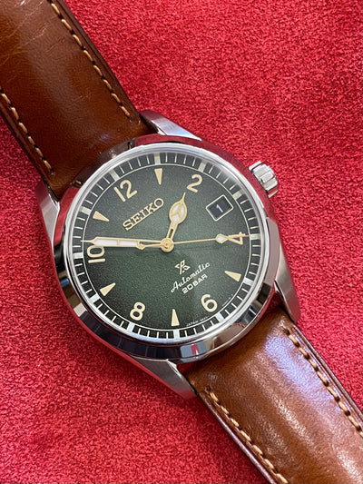 steel wristwatch on green dial and brown leather strap 