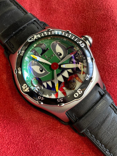 steel wristwatch on decorative dial depicting a smiling shark with propeller as his nose, and black leather