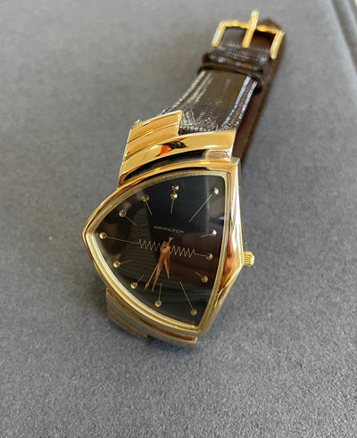 gold tone wristwatch with black dial and brown band